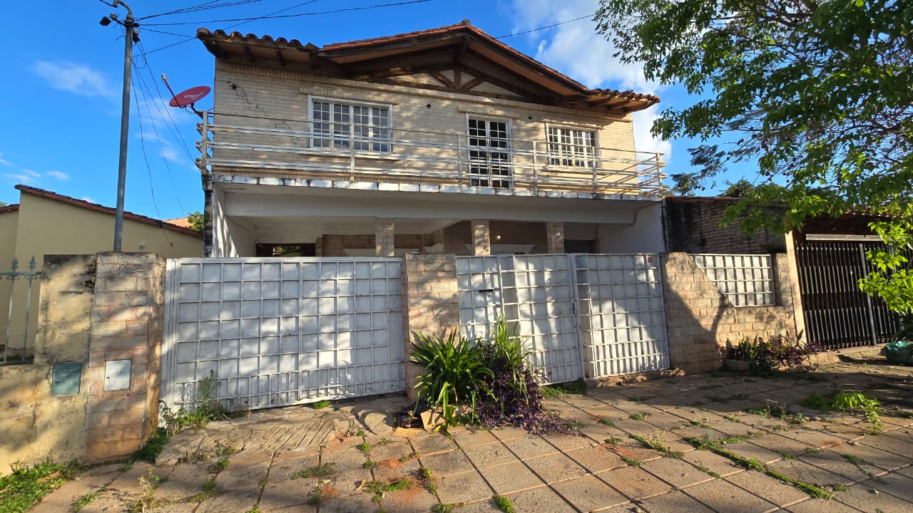 A two-story house with a beige exterior, a tiled roof, and a fenced yard. The house has a balcony on the second floor, and...